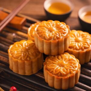 Image of five mooncakes layered on top of each other on a wooden surface with pots of sauce in the background and chopsticks.
