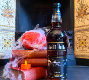 Bottle of Beinn Dubh Scotch whisky placed in front of a fireplace with a pumpkin on top of stacked books and cobwebs. There is an electronic glowing candle on one of the books.