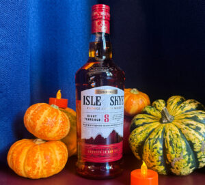 Bottle of Isle of Skye 8 year old Scotch whisky against a navy backdrop. Surrounding the bottle are pumpkins in variosu colours as well as two electonic glowing candles.